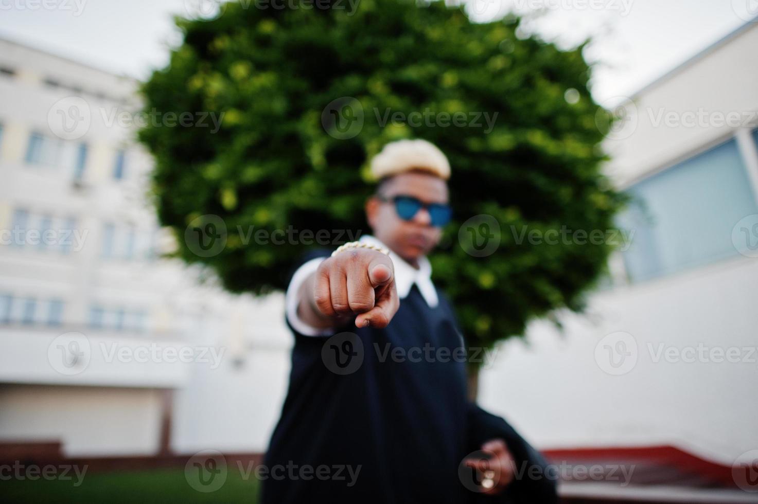 Stylish arabian muslim boy with originally hair and sunglasses posed on streets and show finger at camera. photo