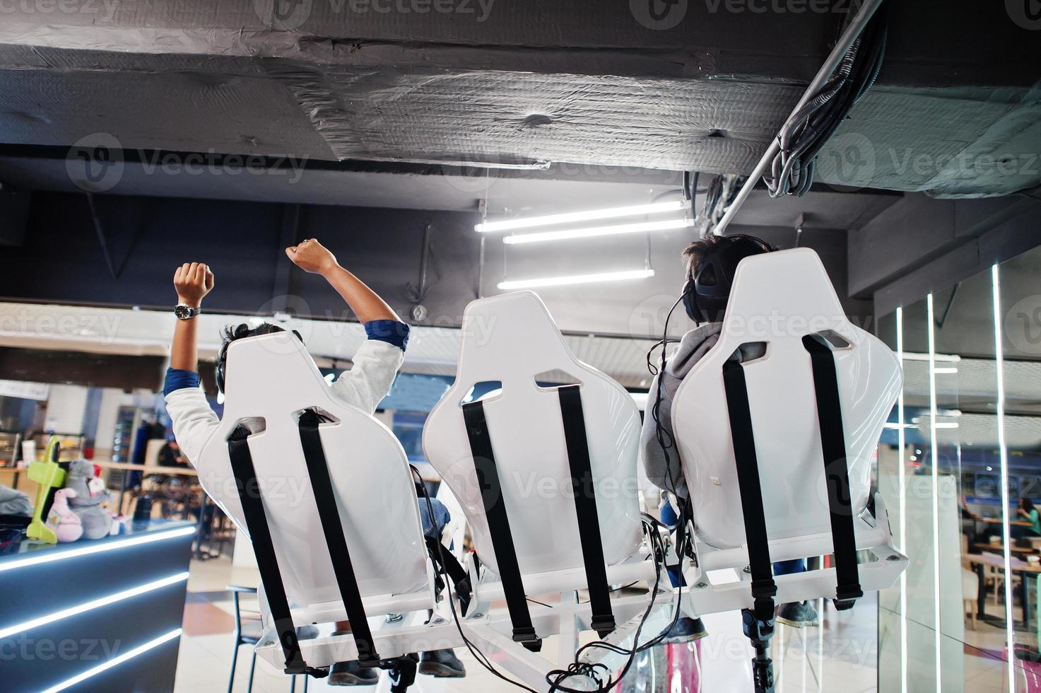 Two young indian people having fun with a new technology of a vr headset at virtual reality simulator.Back of chairs. photo
