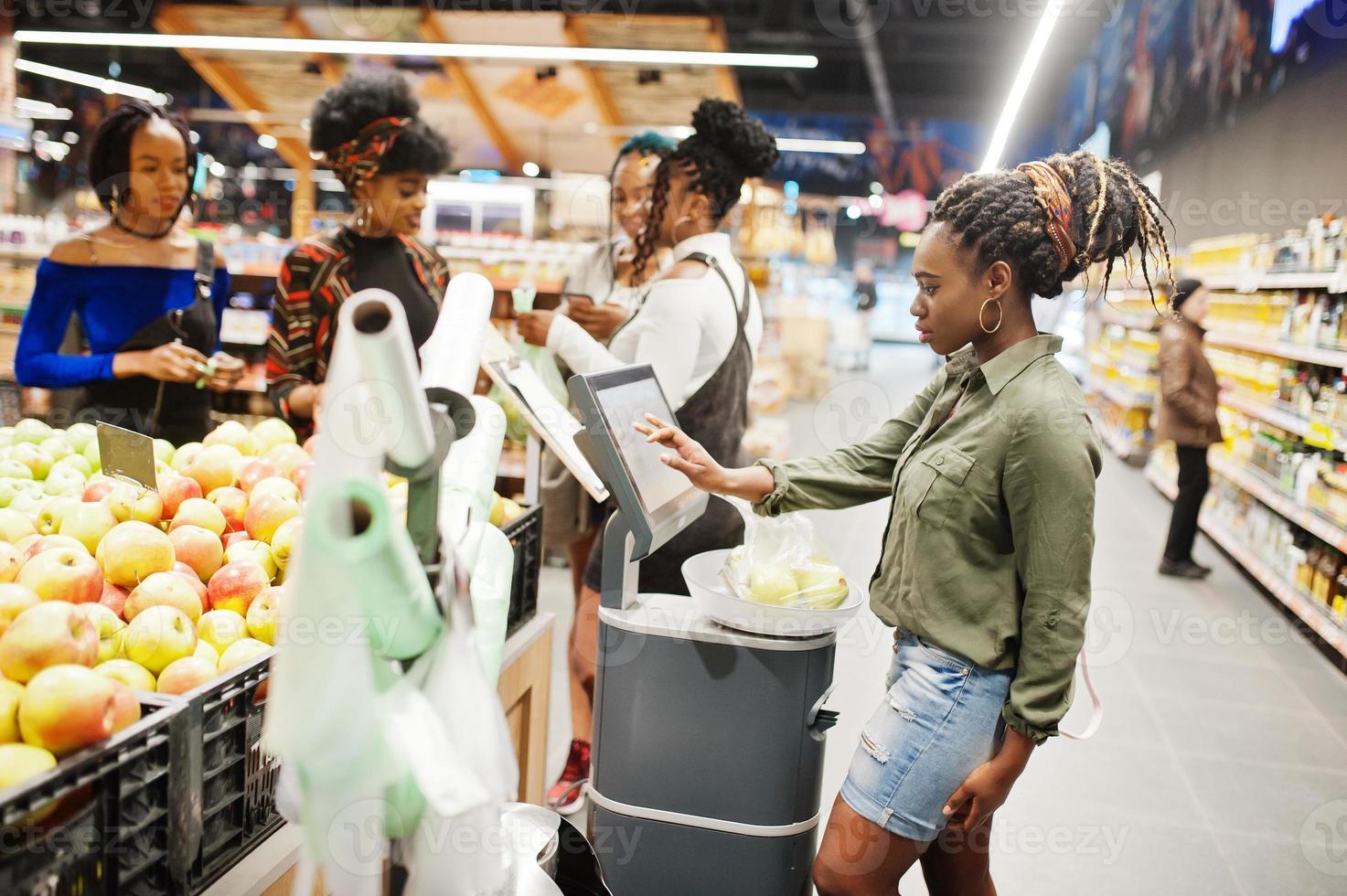 Group of african womans weighs apples in polyethylene bags at supermarket. photo