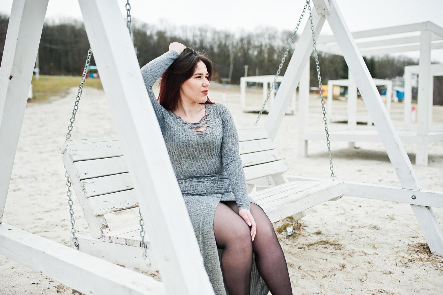 Portrait of brunette girl in gray dress sitting at white wooden construction. photo