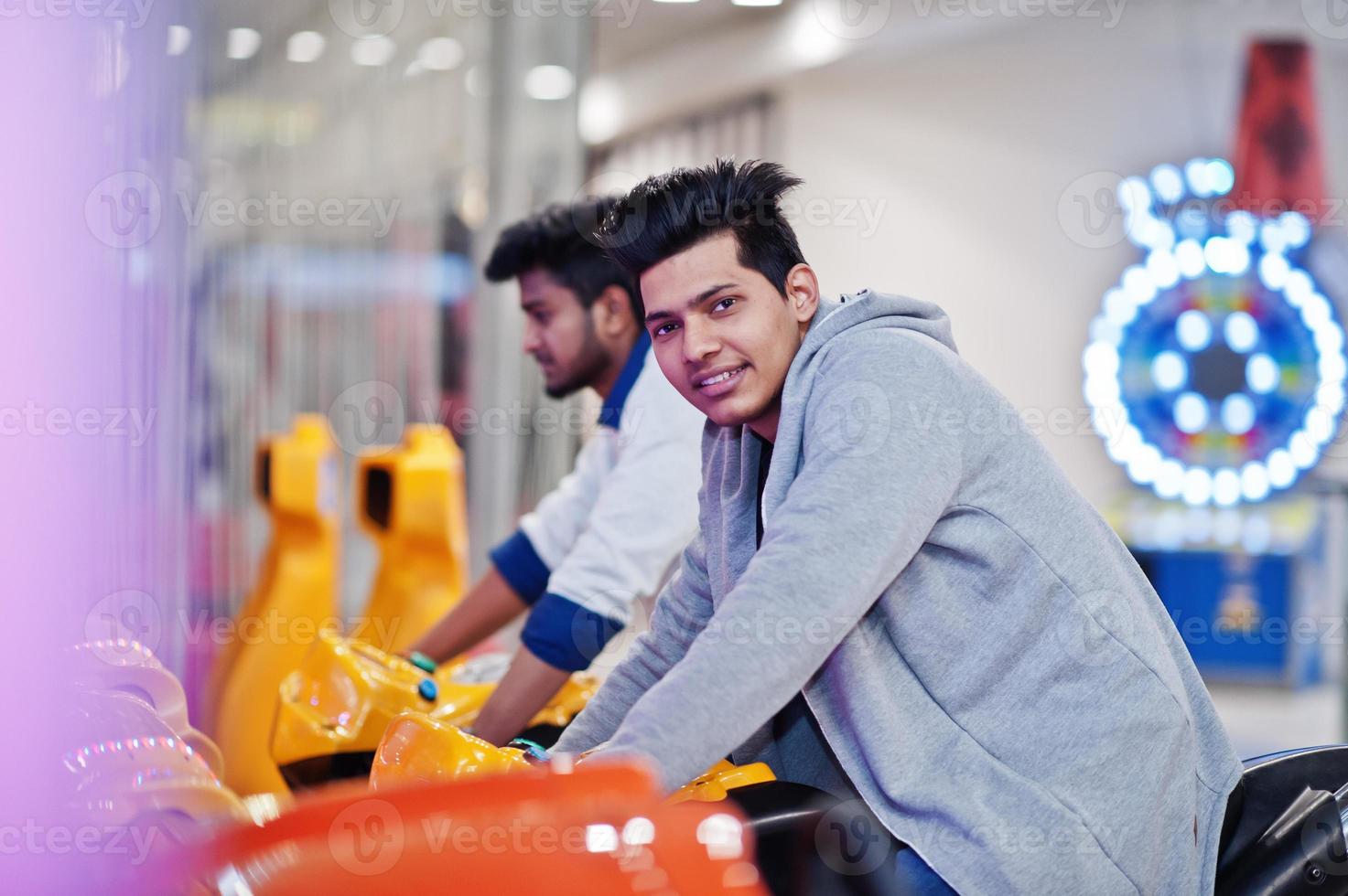 dos chicos asiáticos compiten en la máquina simuladora de carreras de motos del juego arcade de speed rider. foto