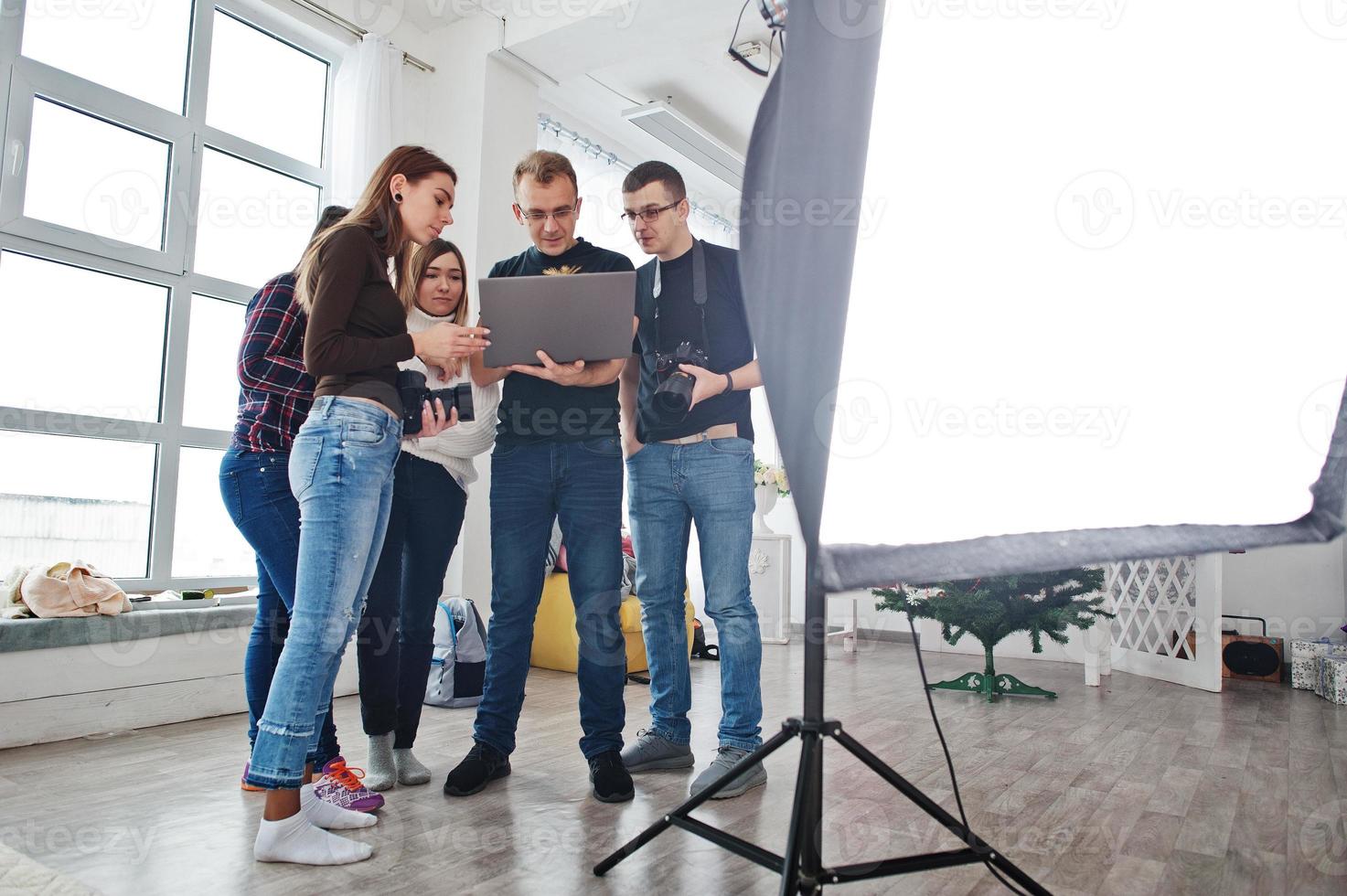 Photographer explaining about the shot to his team in the studio and looking on laptop. Talking to his assistants holding a camera during a photo shoot. Teamwork and brainstorm.