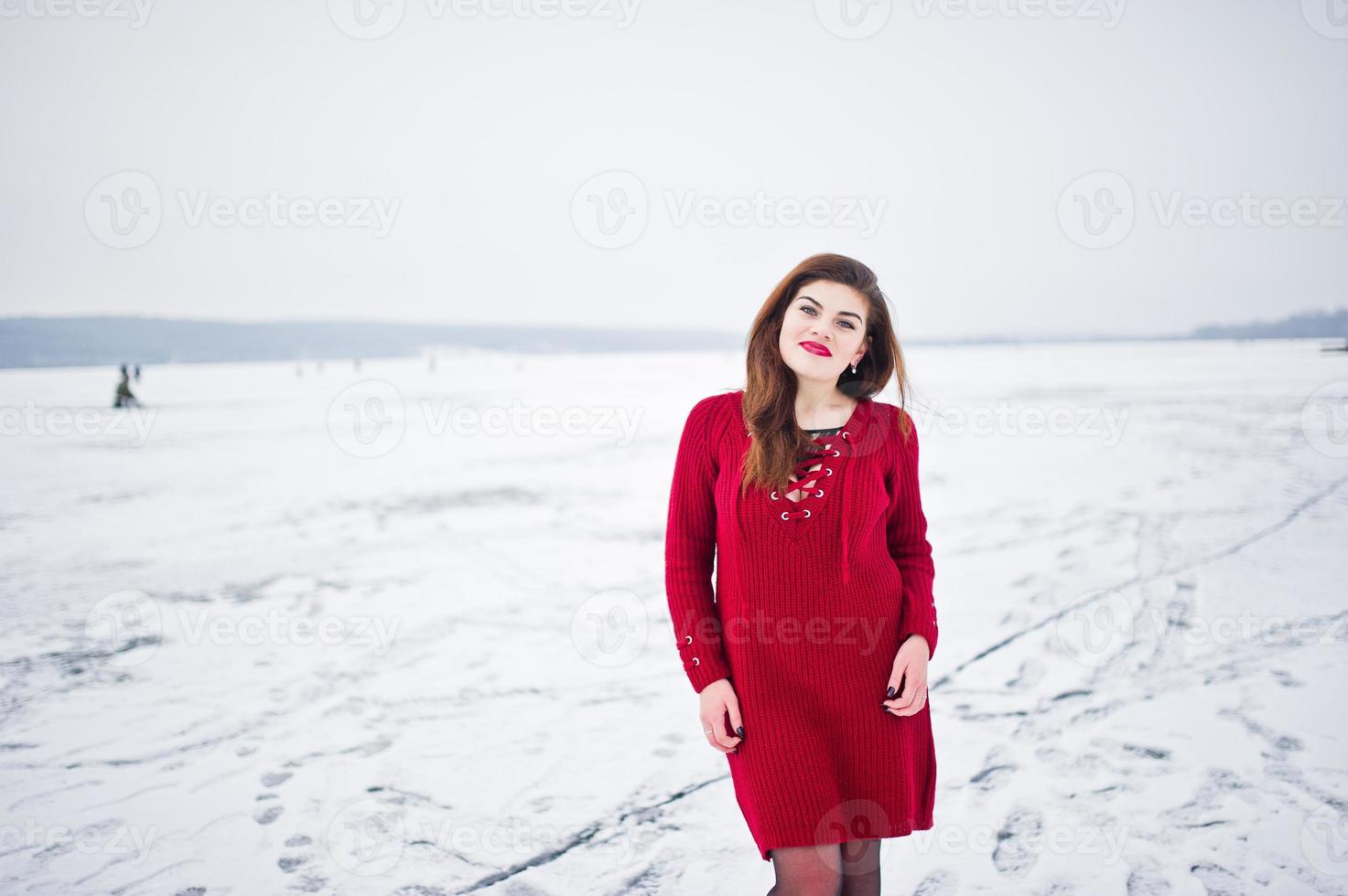 Brunette plus size model at red against frozen lake on winter day. photo