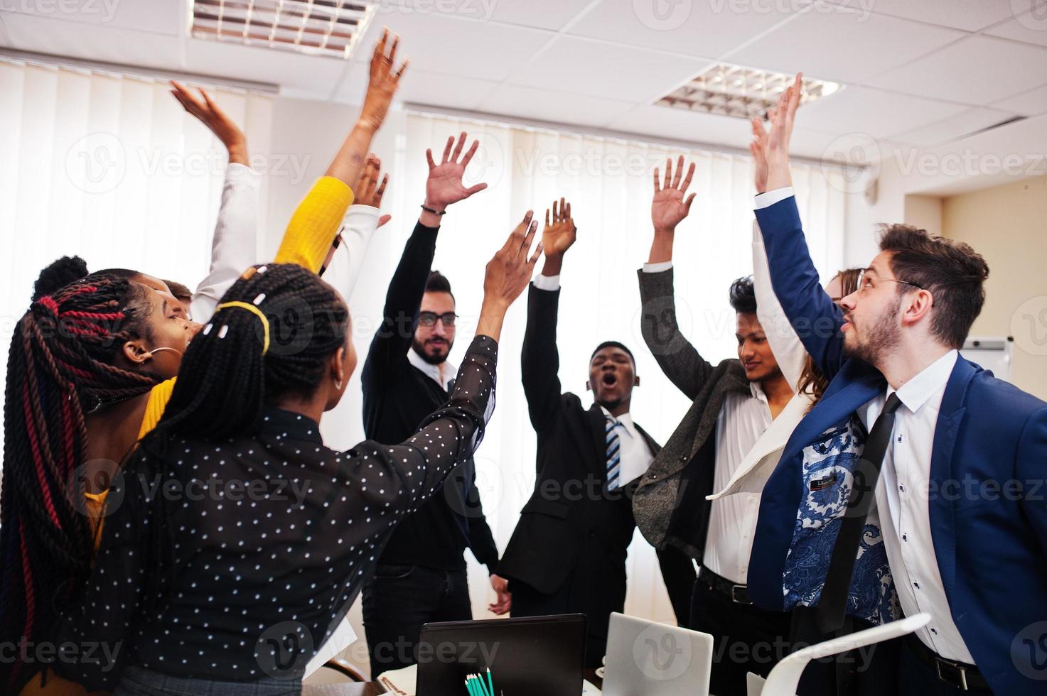 Multiracial business people standing at office and put hands up. Diverse group of employees in formal wear. photo