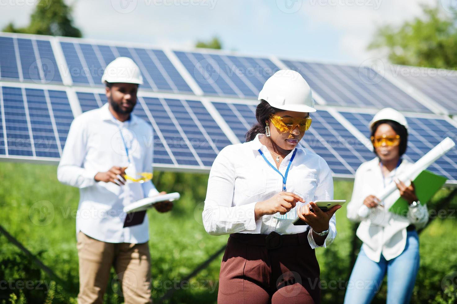 técnico afroamericano comprueba el mantenimiento de los paneles solares. grupo de tres ingenieros negros reunidos en la estación solar. foto