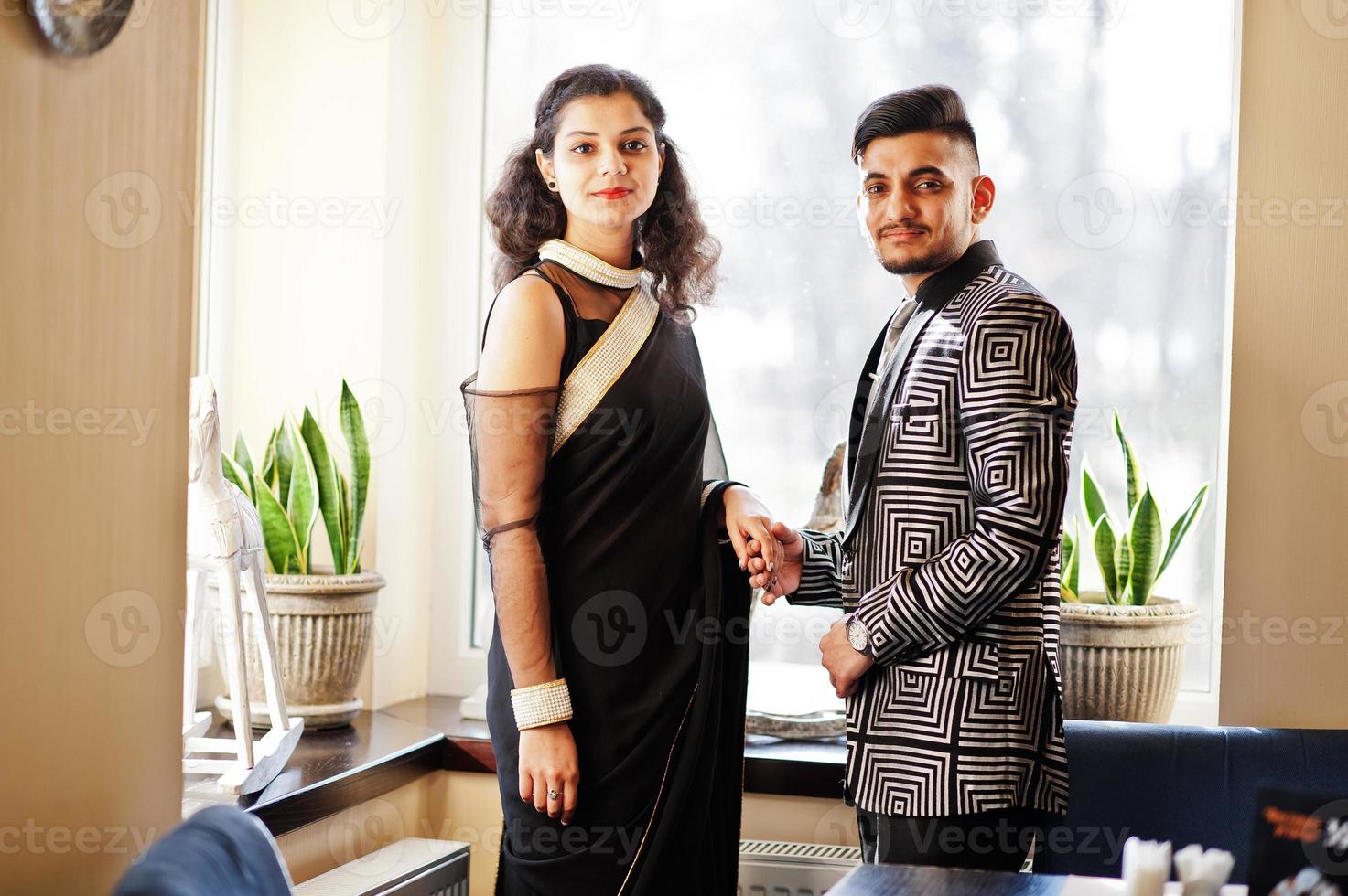 Lovely indian couple in love, wear at saree and elegant suit, posed on restaurant against window. photo