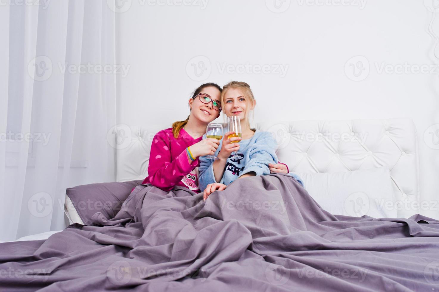 Two friends girls in pajamas having fun on bed at room. photo