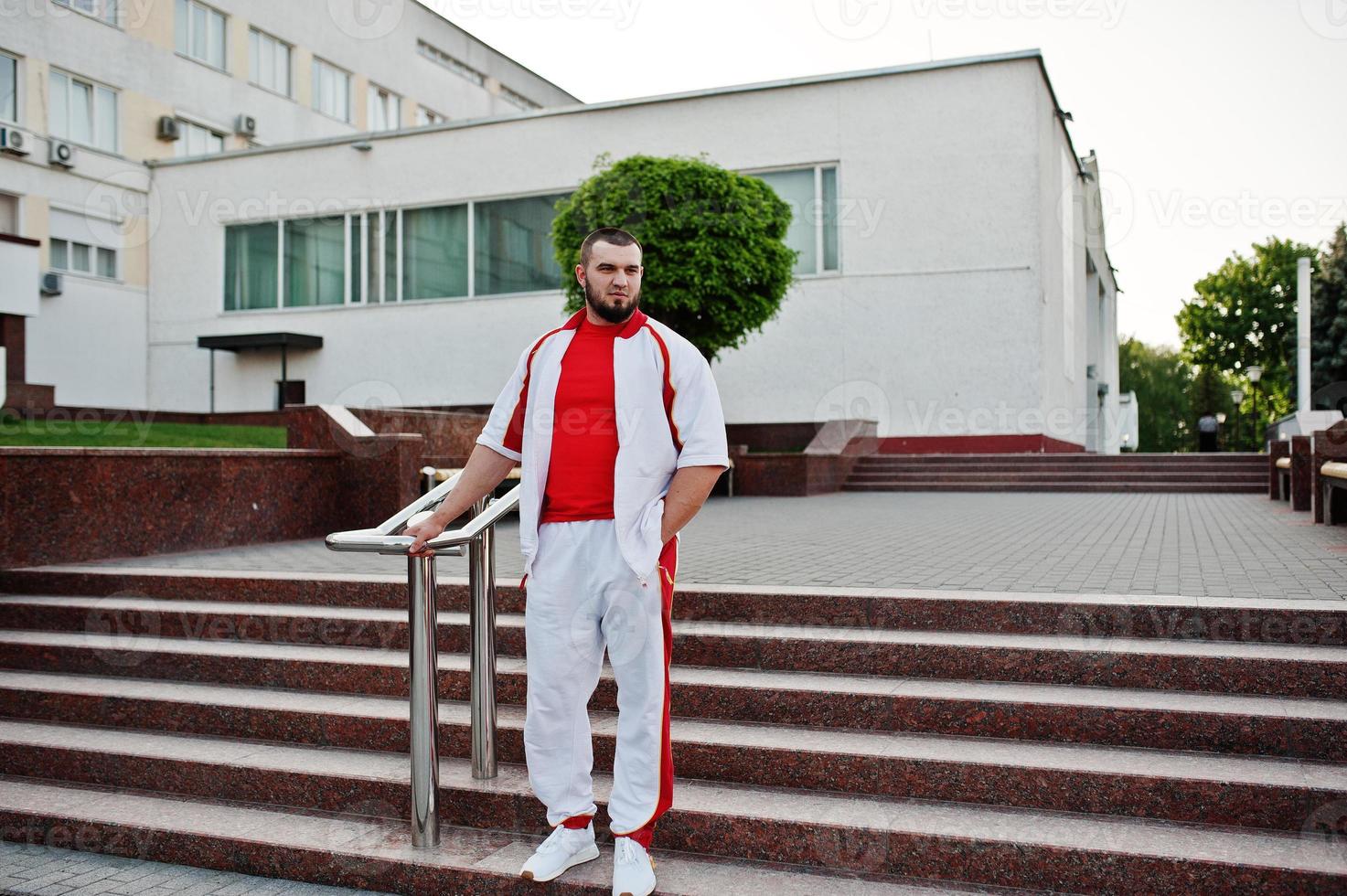 joven musculoso barbudo brutal vestido con traje deportivo blanco con camisa roja. foto