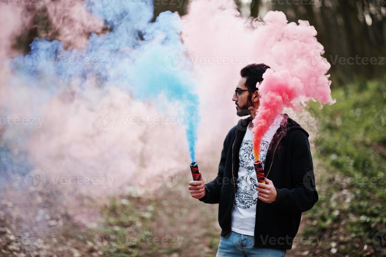 Street style arab man in eyeglasses hold hand flare with red and blue smoke grenade bomb. photo