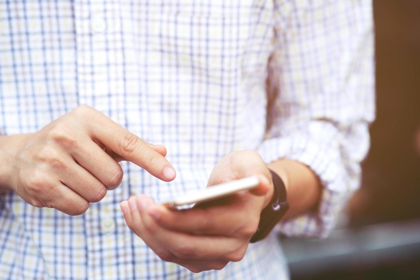 joven usa camisa a cuadros. cierre la mano usando el teléfono celular durante el descanso en el sofá. sentado viendo un mensaje en un teléfono inteligente móvil durante el descanso, relájese. enfoque suave. foto