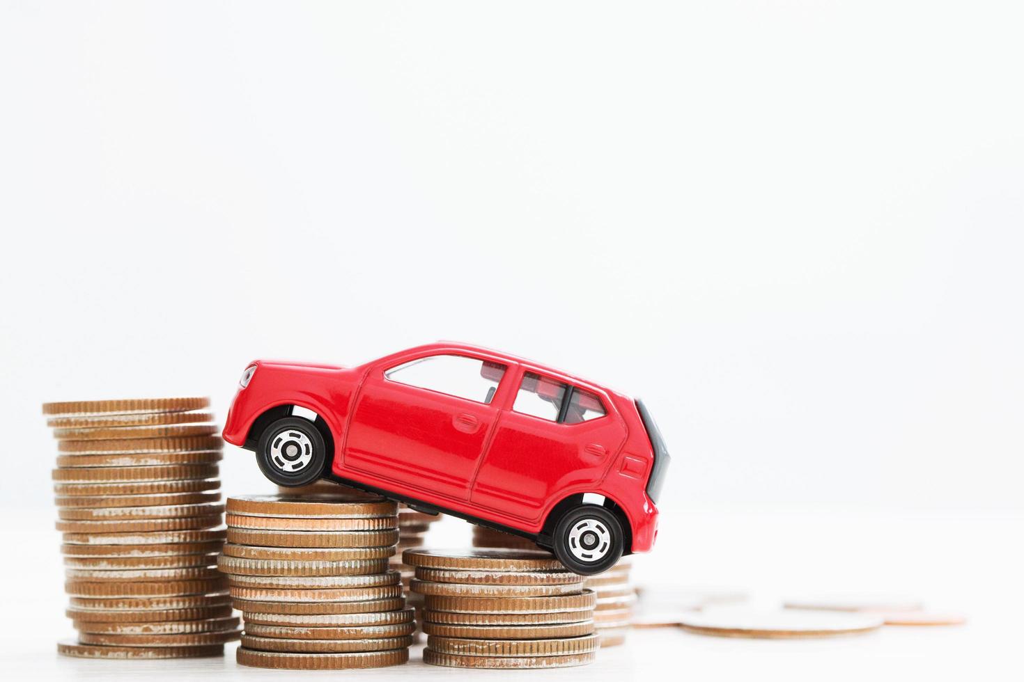 pequeño coche rojo sobre un montón de monedas apiladas. para préstamos bancarios costos financiar. seguro, compra de concepto de financiación de automóviles. comprar y pagar a plazos el pago inicial de un coche. foto