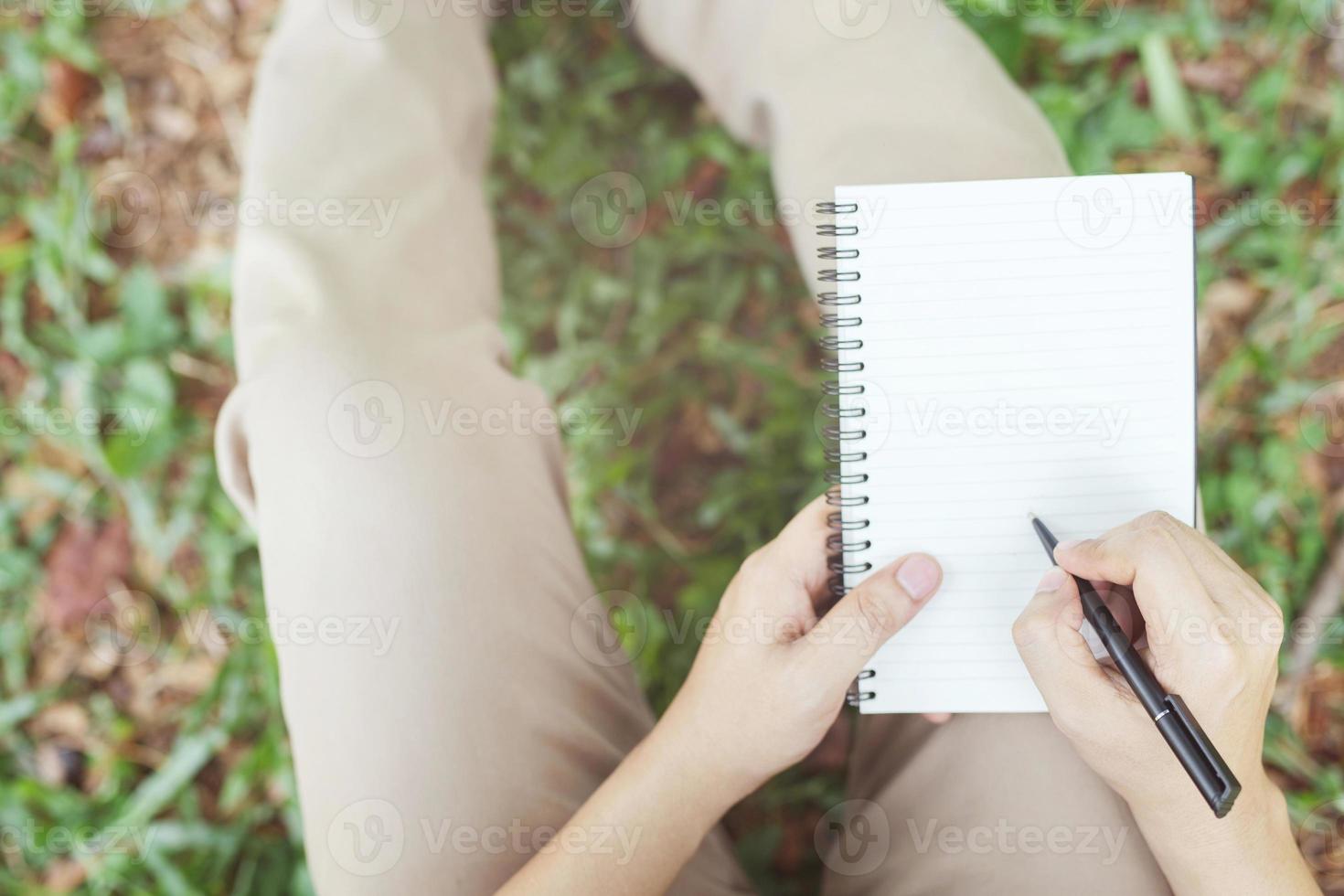 close up hand young man are using pen writing Record Lecture note pad into the book sitting on the chair outdoor. Blank book page copy  write a message. photo