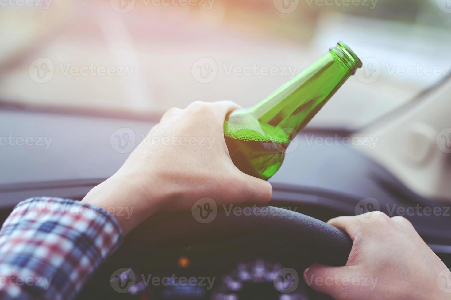 close up hand Drunk young man while driving a car with a bottle of beer. Don't drink and drive concept. Driving while intoxicated the danger may be a death. photo