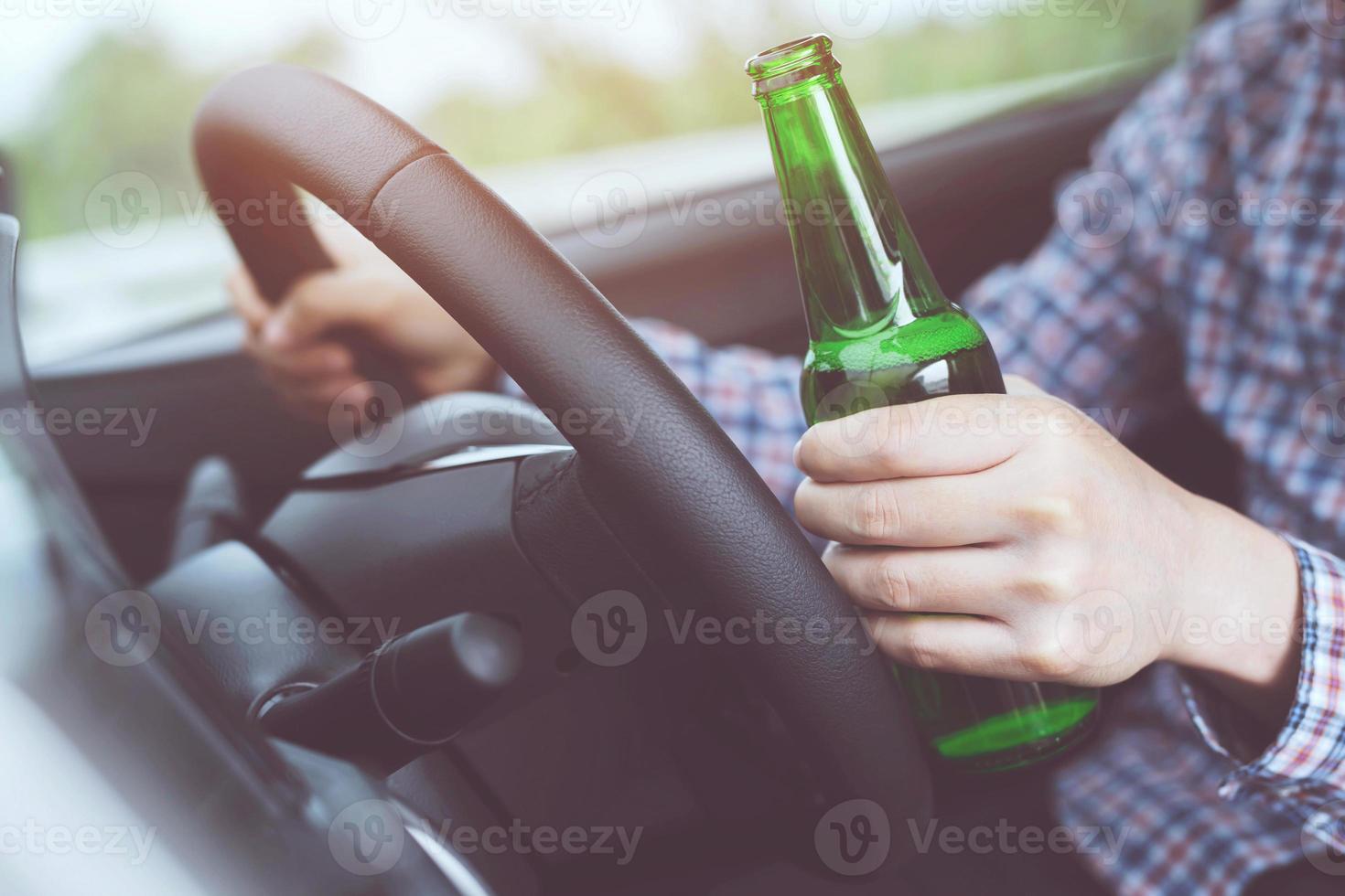 close up hand Drunk young man while driving a car with a bottle of beer. Don't drink and drive concept. Driving while intoxicated the danger may be a death. photo