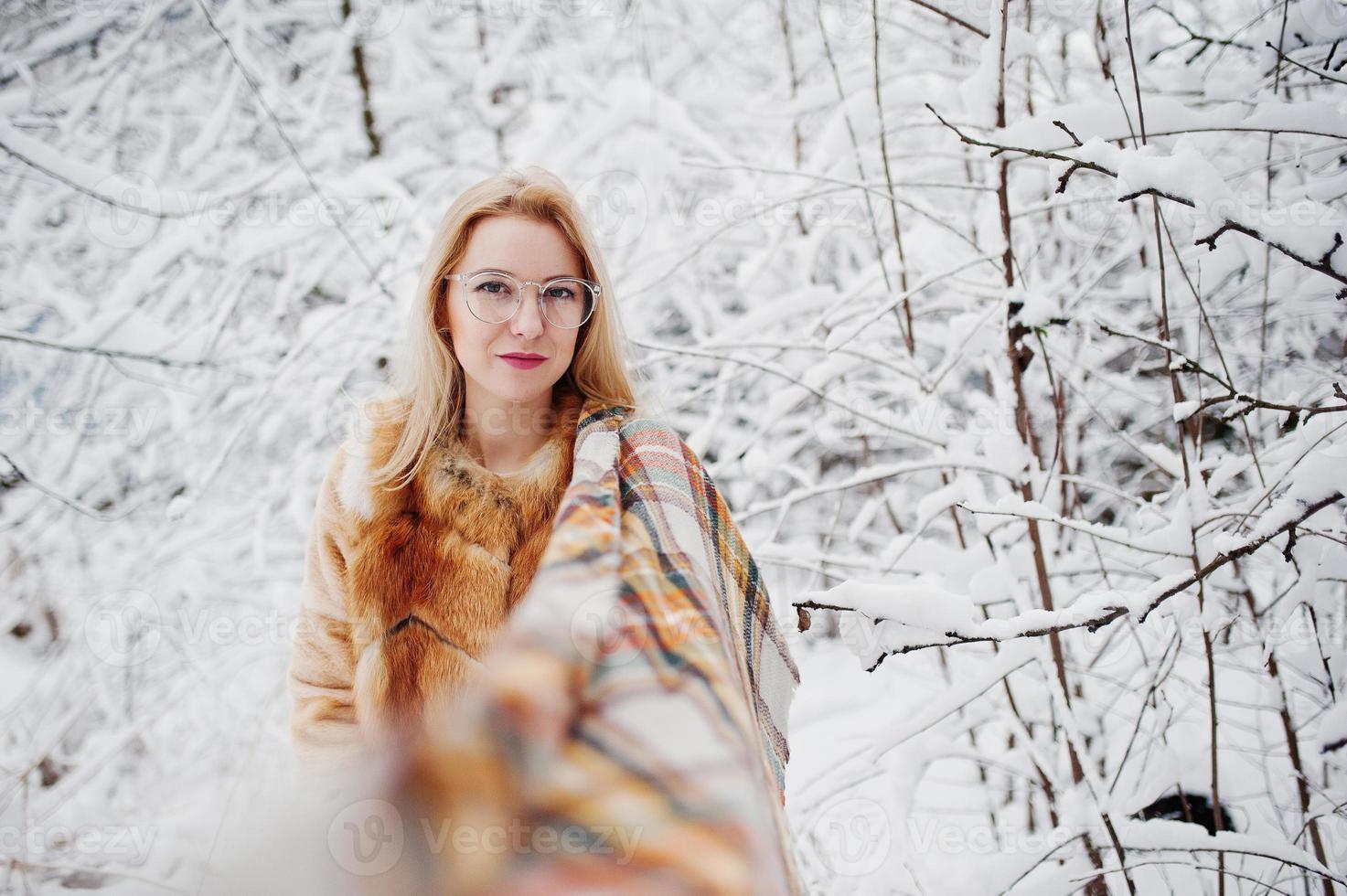 Portraiy of blonde girl in glasses, red fur coat and scarf at winter day. photo