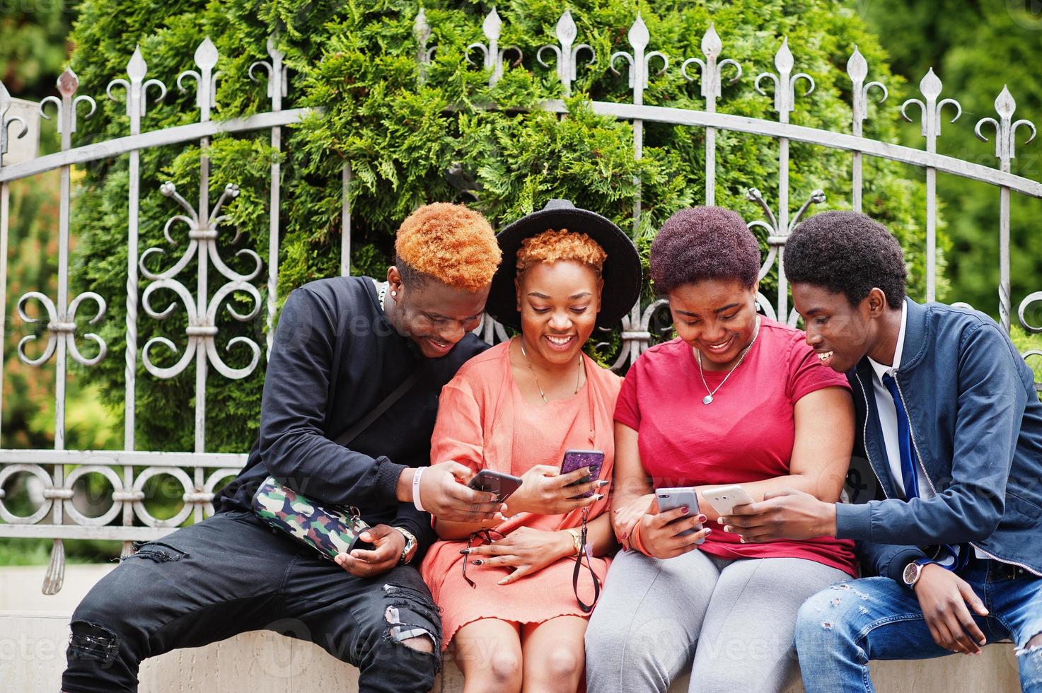 Four african friends having fun outdoors. Two black girls with guys with mobile phones. photo