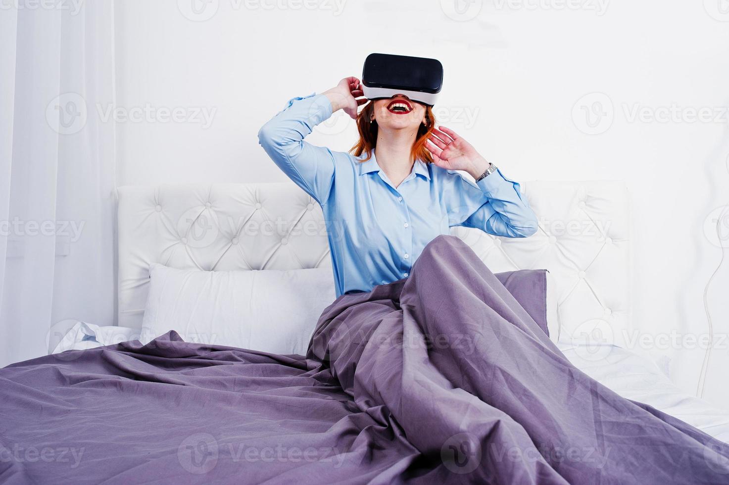 Red haired girl in bed with vr glasses at studio room. photo