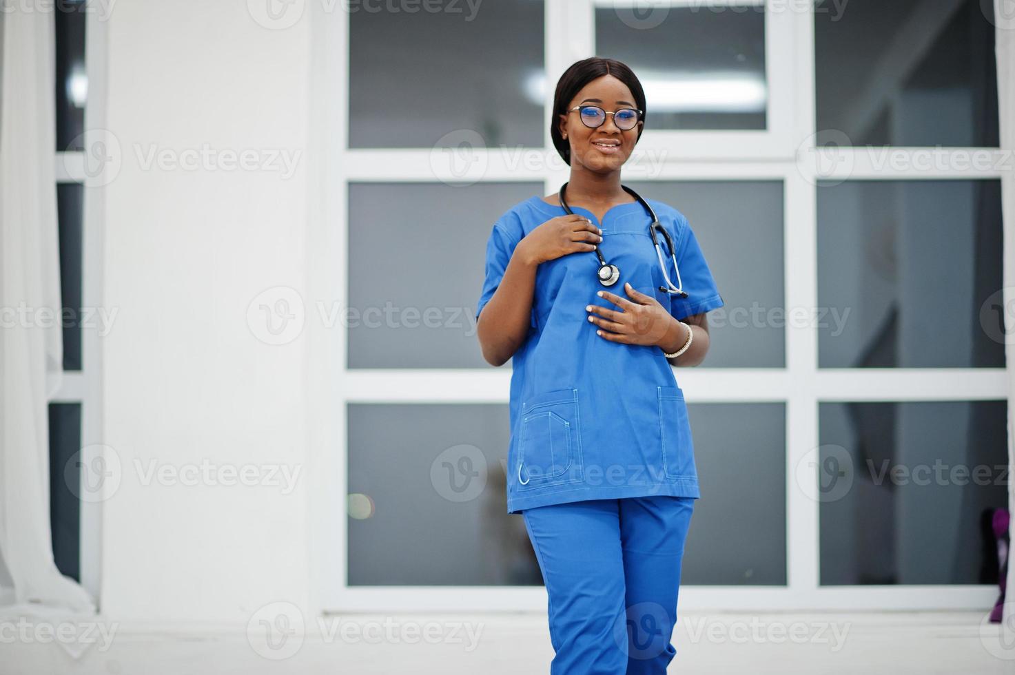 retrato de una joven y feliz doctora afroamericana pediatra con uniforme azul y estetoscopio contra la ventana del hospital. cuidado de la salud, médico, especialista en medicina - concepto. foto