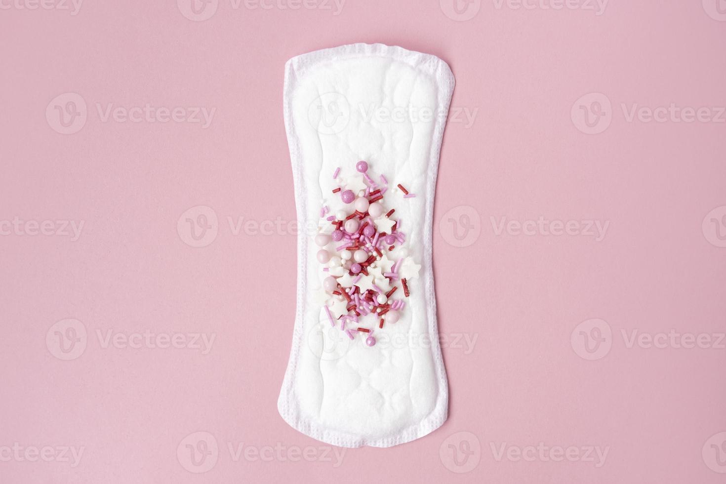 almohadilla menstrual con confeti rojo como gotas de sangre sobre fondo rosa pastel. concepto minimalista de higiene femenina durante la menstruación. vista superior. foto