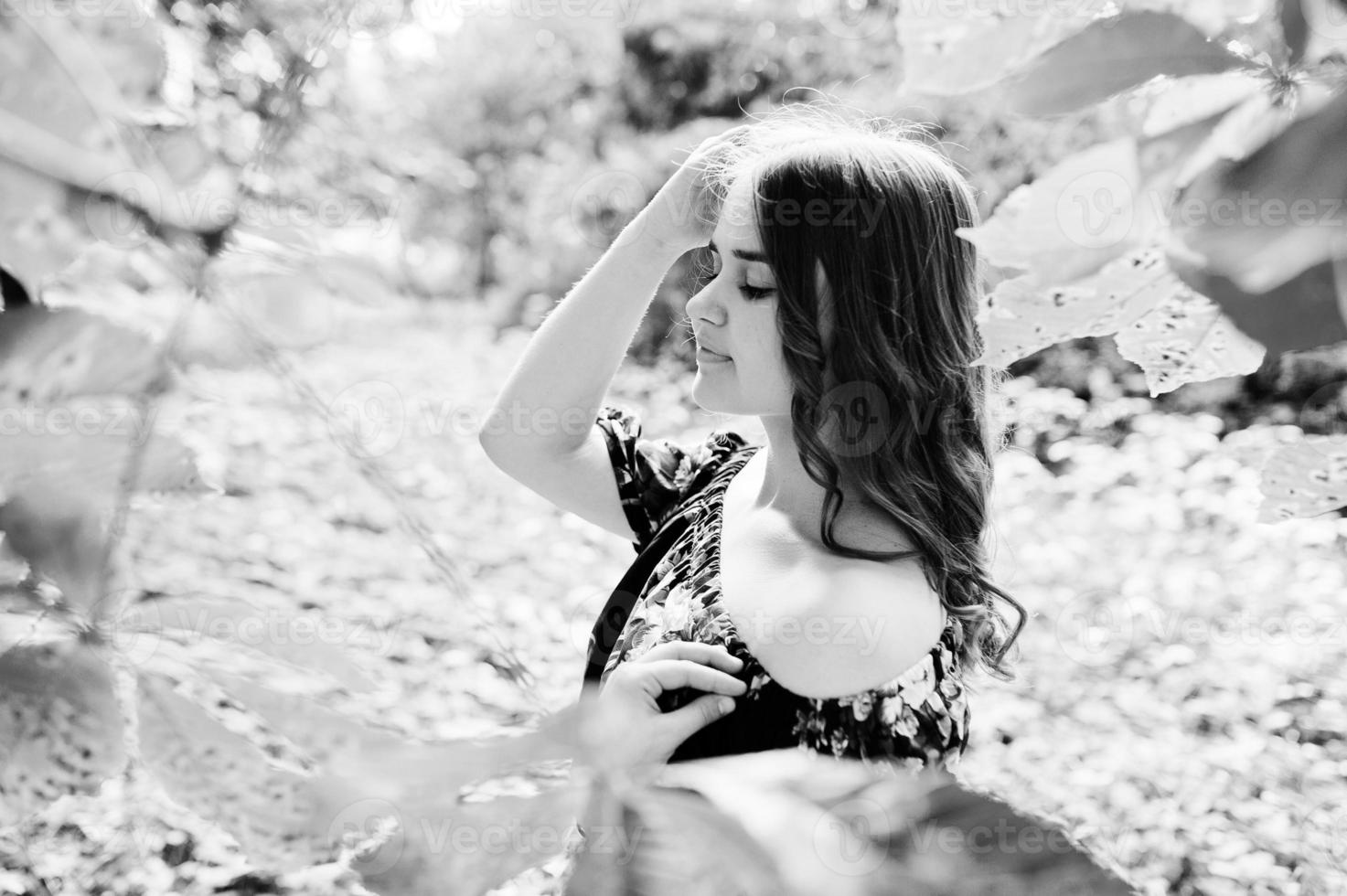 Close-up portrait of a beautiful brunette in dress next to the leaves. photo
