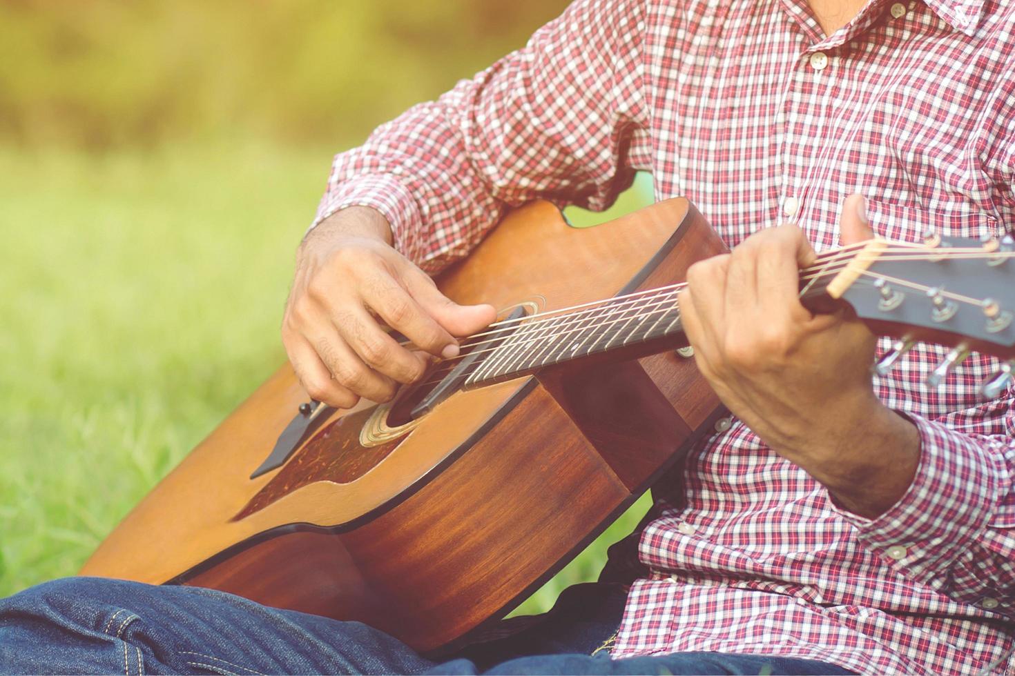 Stylish hipster guy Acoustic Guitar Playing by hand. Artist Men  musician Playing Acoustic Guitar in public park. photo