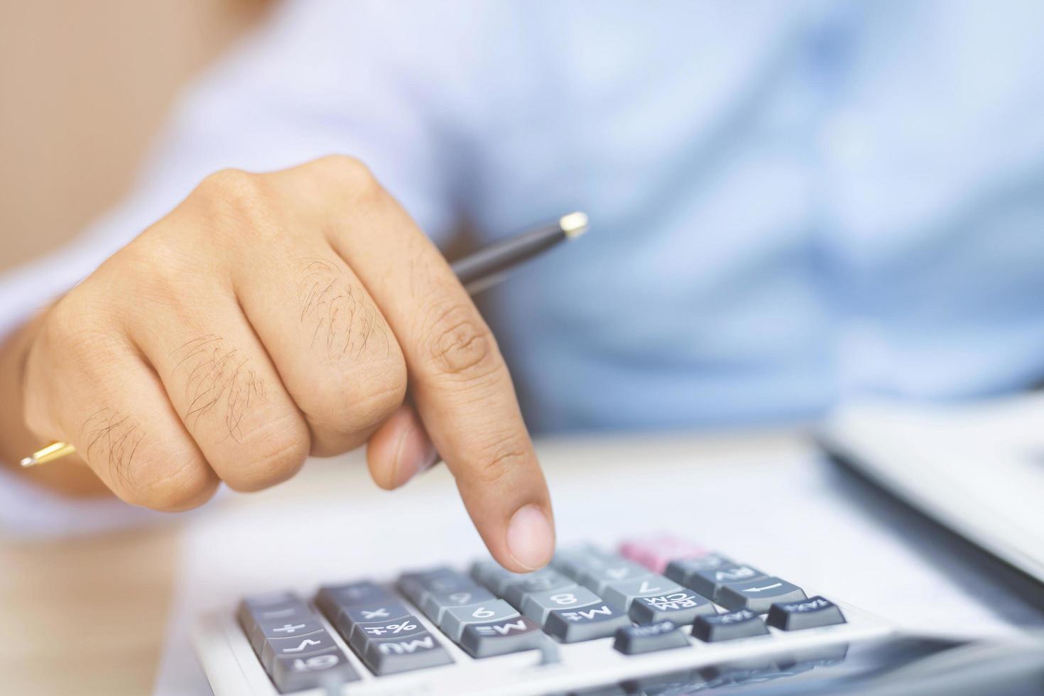 Close up of businessman or accountant hand holding pencil working on calculator to calculate financial data report, accountancy document and laptop computer at office, business concept photo