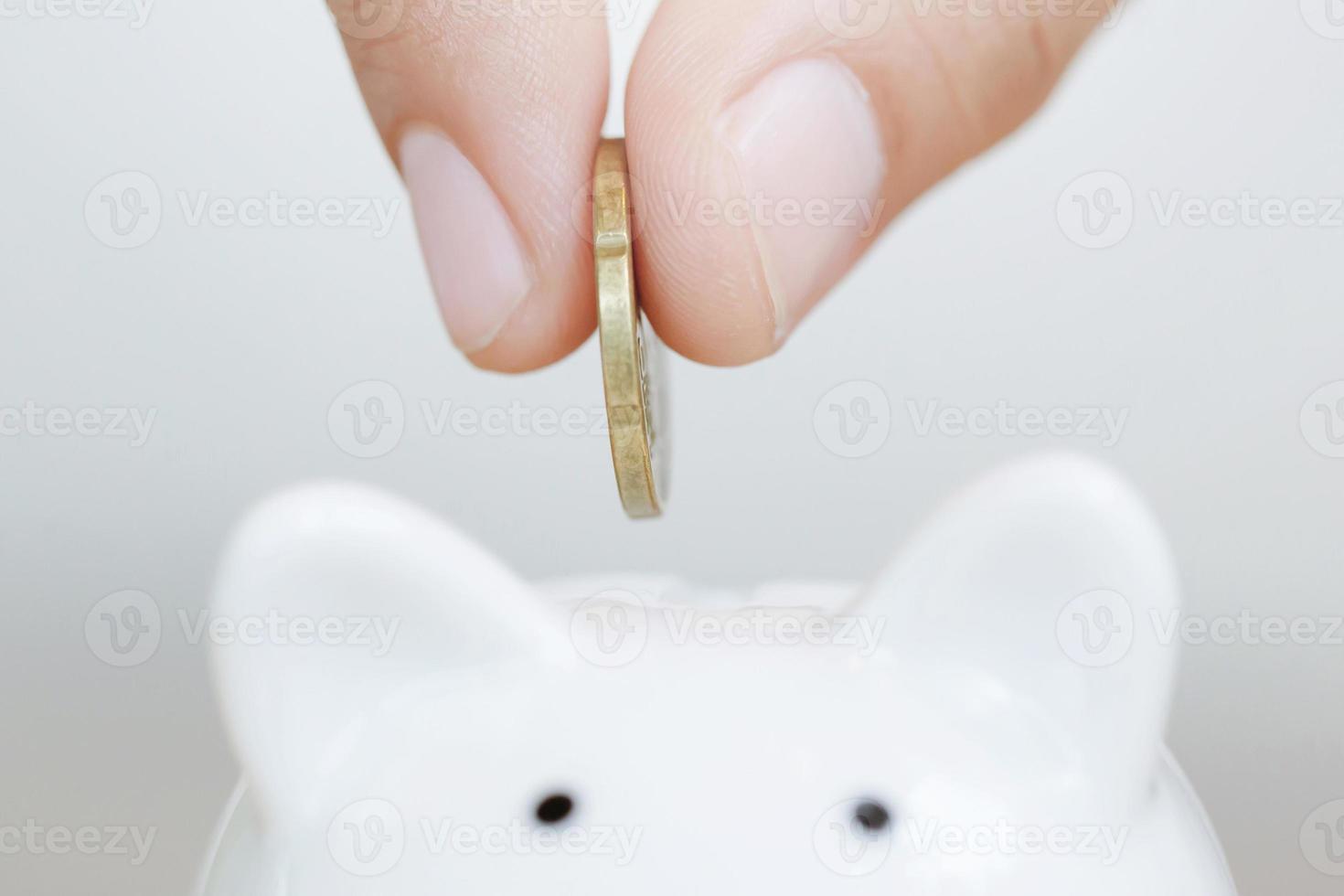 Saving, hand putting golden coin in piggy bank money box white. photo