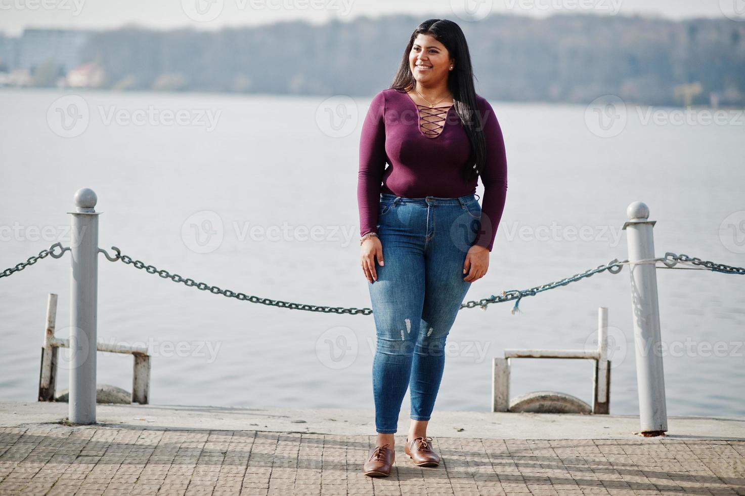 Pretty latino xxl model girl from Ecuador wear on violet blouse posed against lake. photo