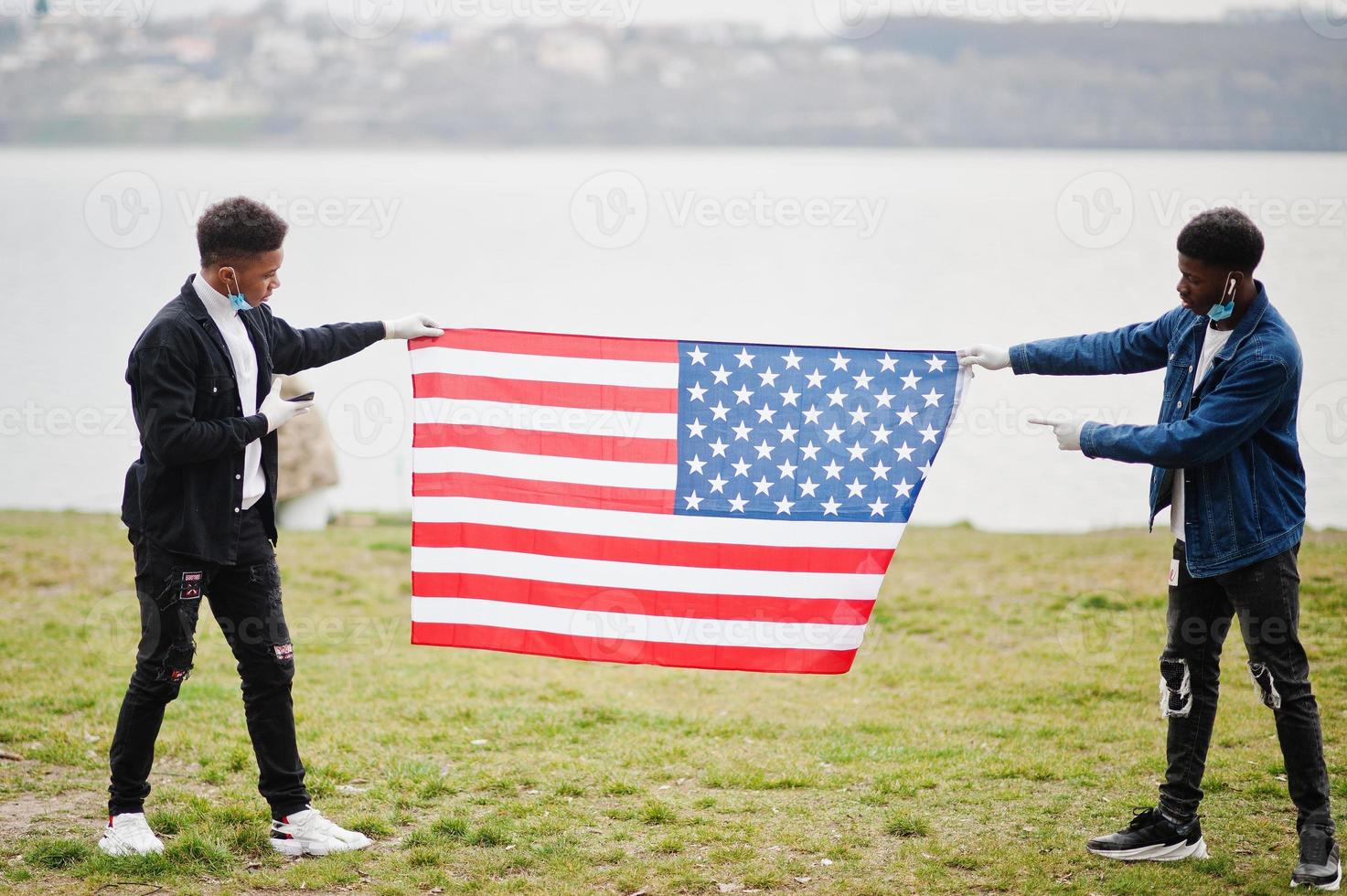 Two african teenagers friends with american flag at park wearing medical masks protect from infections and diseases coronavirus virus quarantine. photo