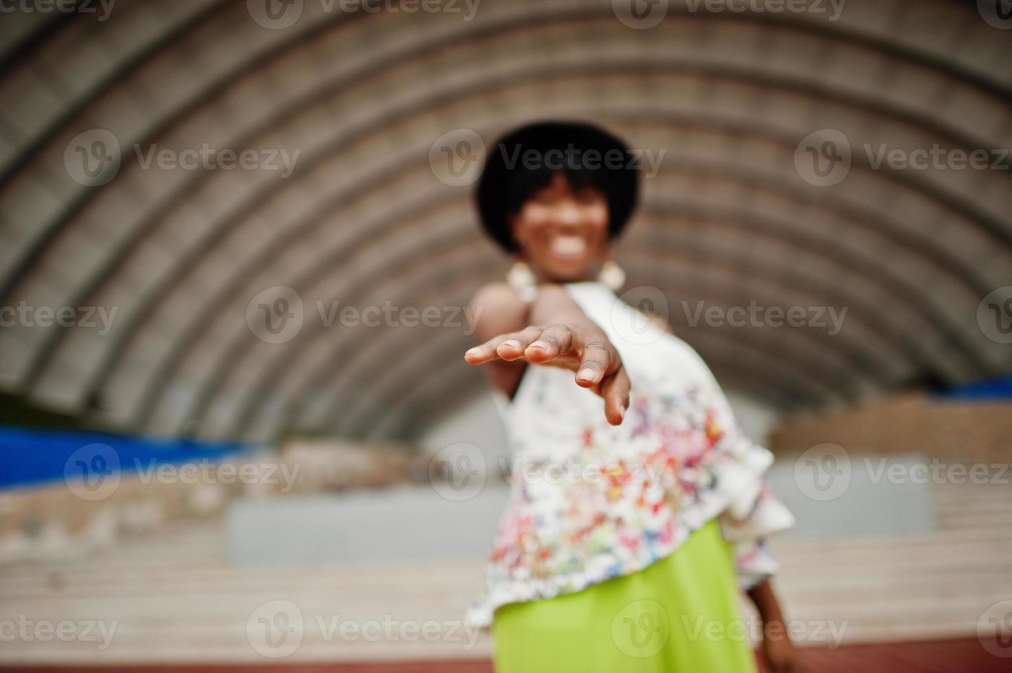 Amazing african american model woman in green pants and black hat posed outdoor against arena hall. photo