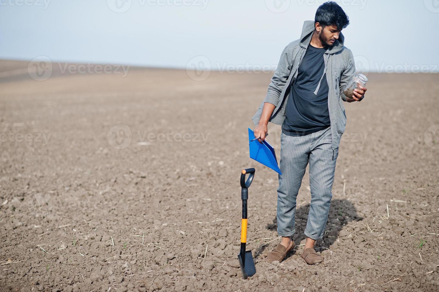 South asian agronomist farmer with shovel inspecting black soil. Agriculture production concept. photo