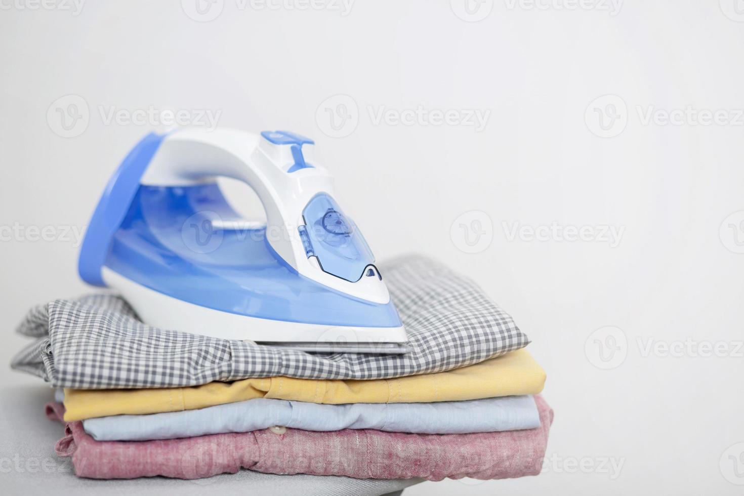 Electric iron and pile of clean clothes shirts variety of colors on ironing board. Leave space to write side text. photo