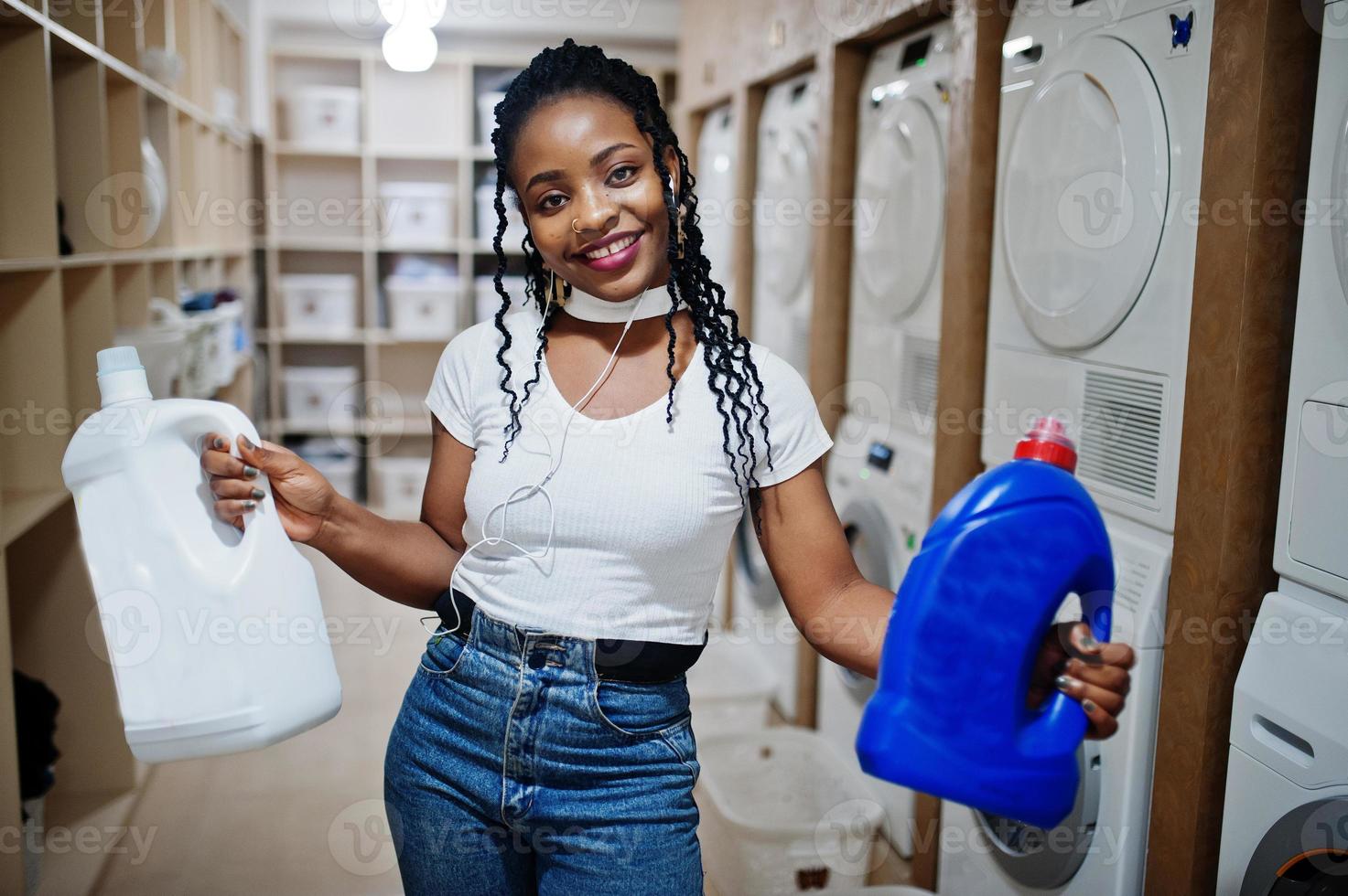 Cheerful african american woman hold detergent near washing machine in the self-service laundry. photo