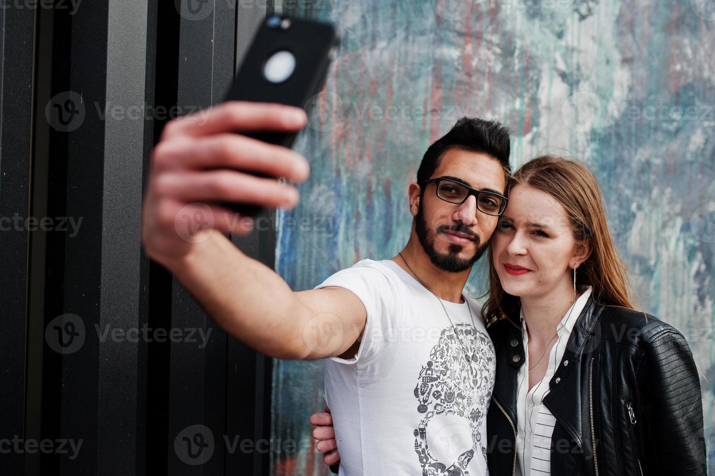 genial pareja multirracial posando contra la pared y haciendo selfie juntos. foto