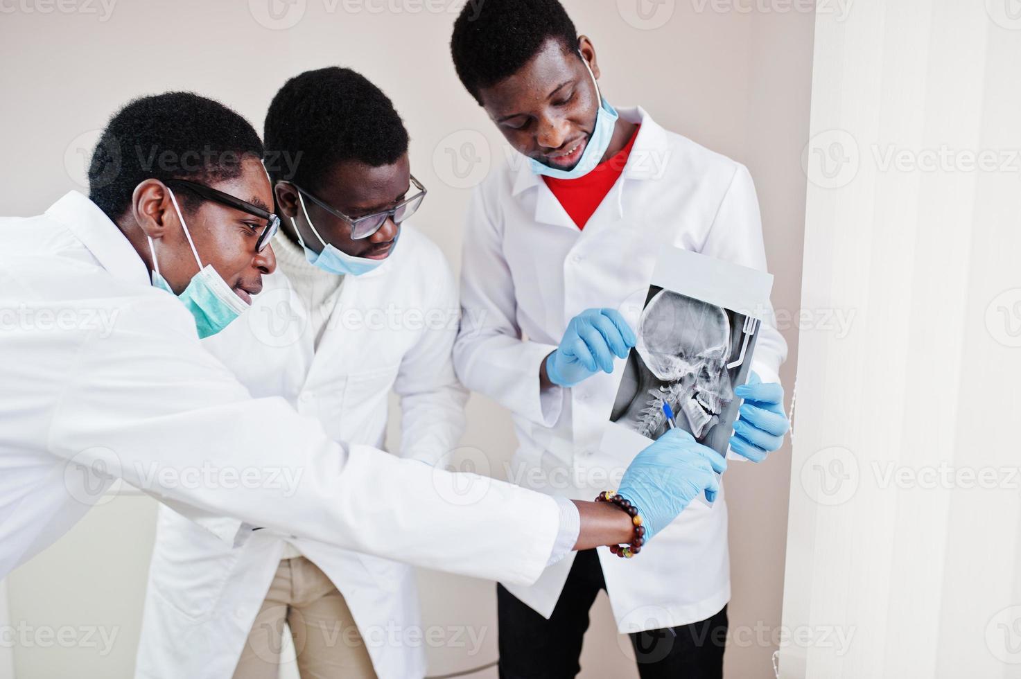 tres médicos afroamericanos trabajando, discutiendo con colegas en la clínica y señalando el cráneo de rayos x. foto