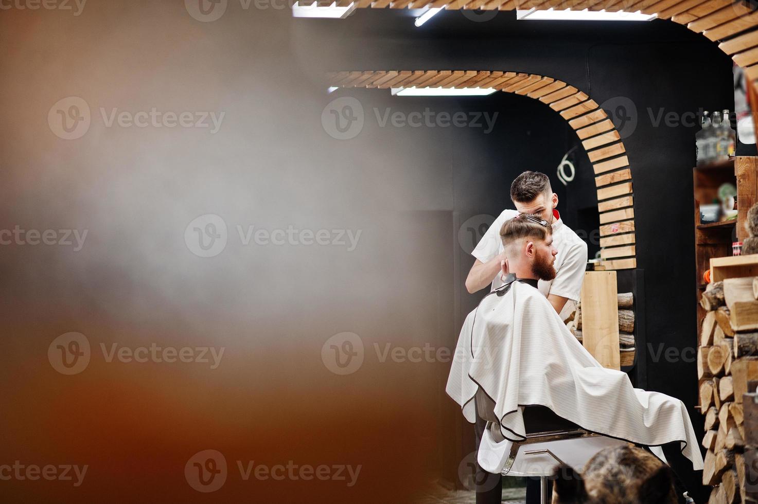 un joven barbudo que se corta el pelo con un peluquero mientras se sienta en una silla en la barbería. alma de barbero. foto