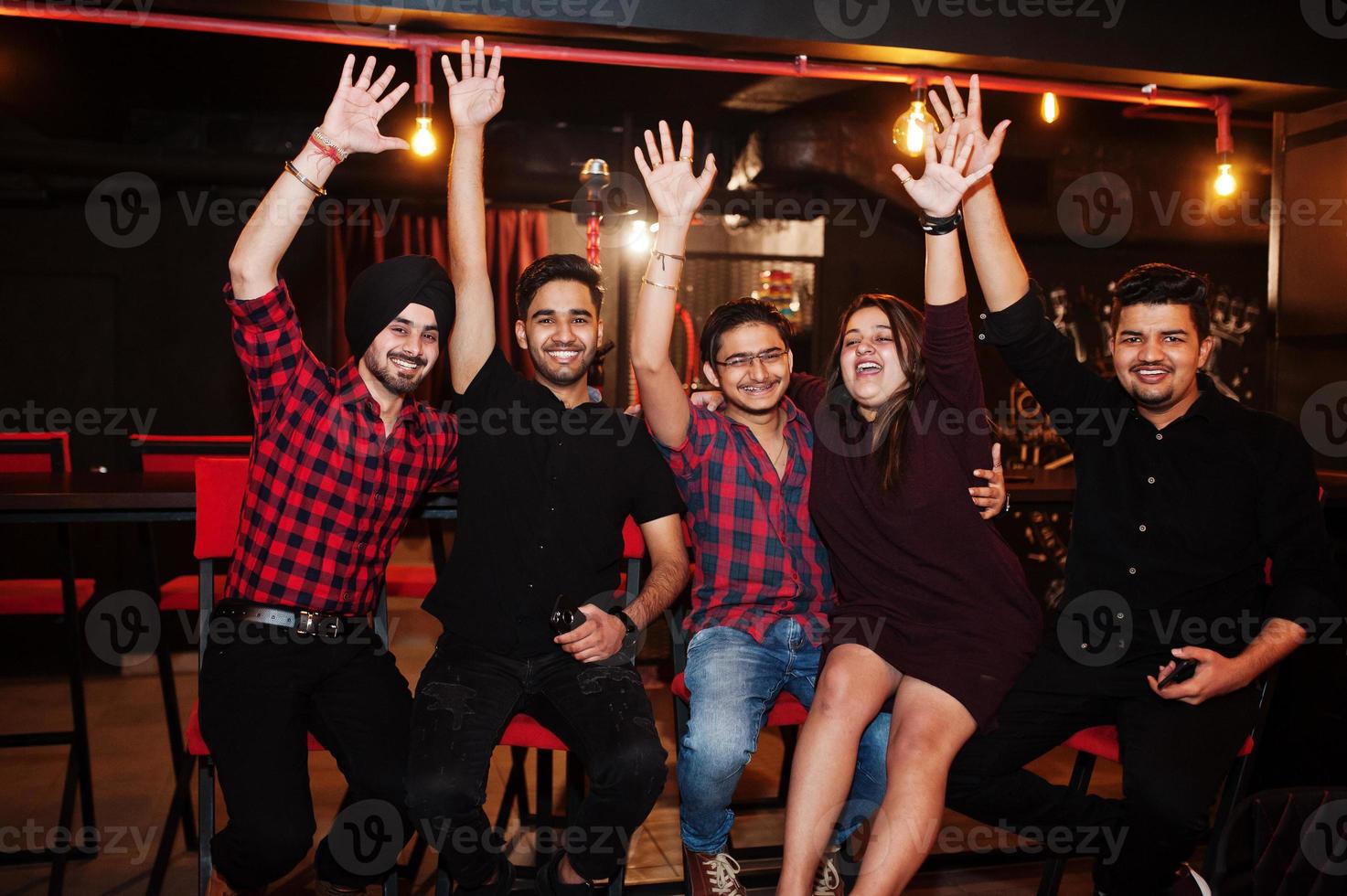 Group of indian friends sitting at lounge bar, having fun and rest. Hands up. photo