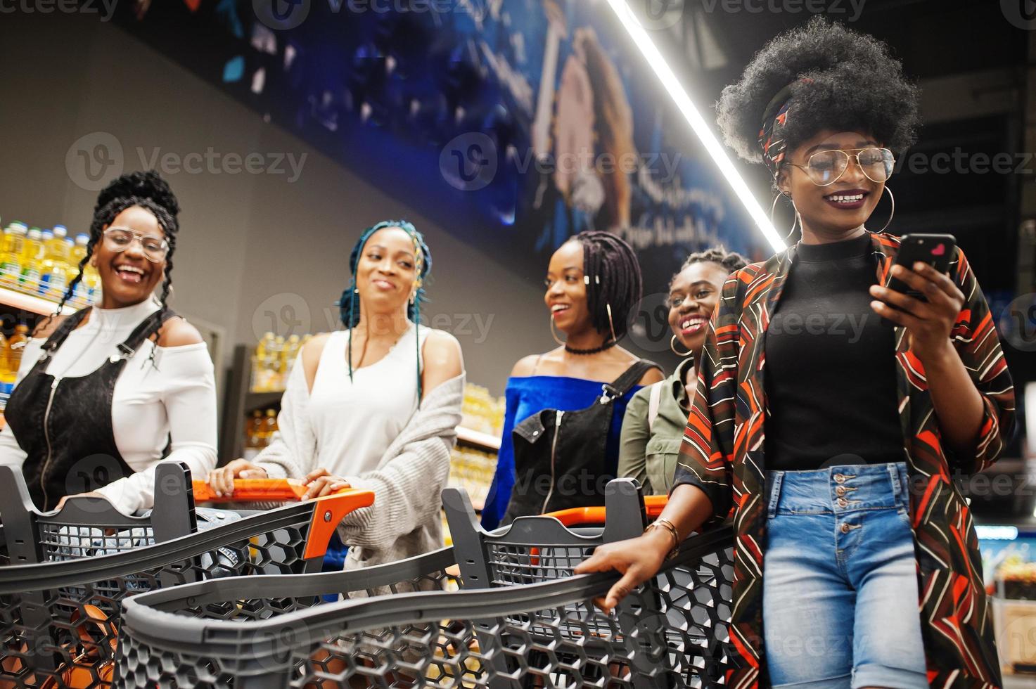 grupo de cinco mujeres africanas caminando en un supermercado con carritos de compras. foto