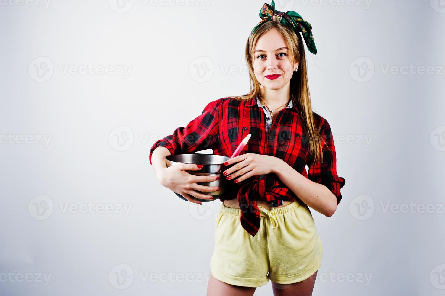 Young funny housewife in checkered shirt and yellow shorts pin up style with saucepan and kitchen spoon isolated on white background. photo