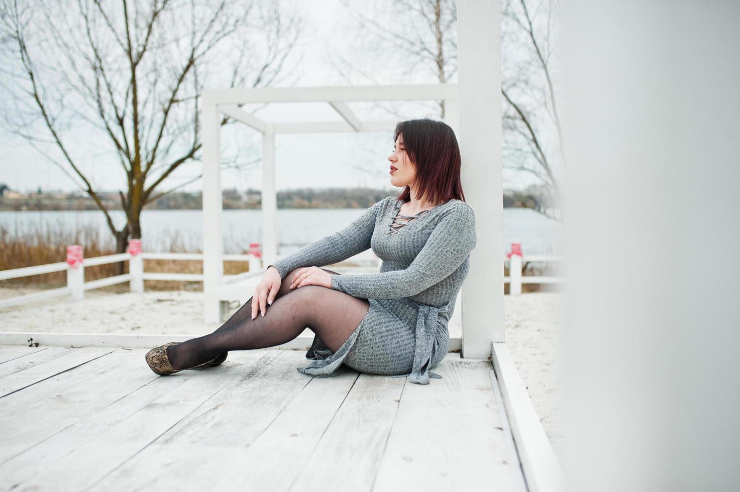 Portrait of brunette girl in gray dress sitting at white wooden construction. photo