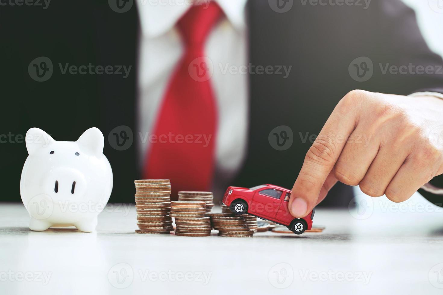 Business man in suit open hand prop up hug model of toy car on over a lot money of stacked coin insurance loan and buying car finance concept. buy and installment down payment a car. Piggy Bank saving photo