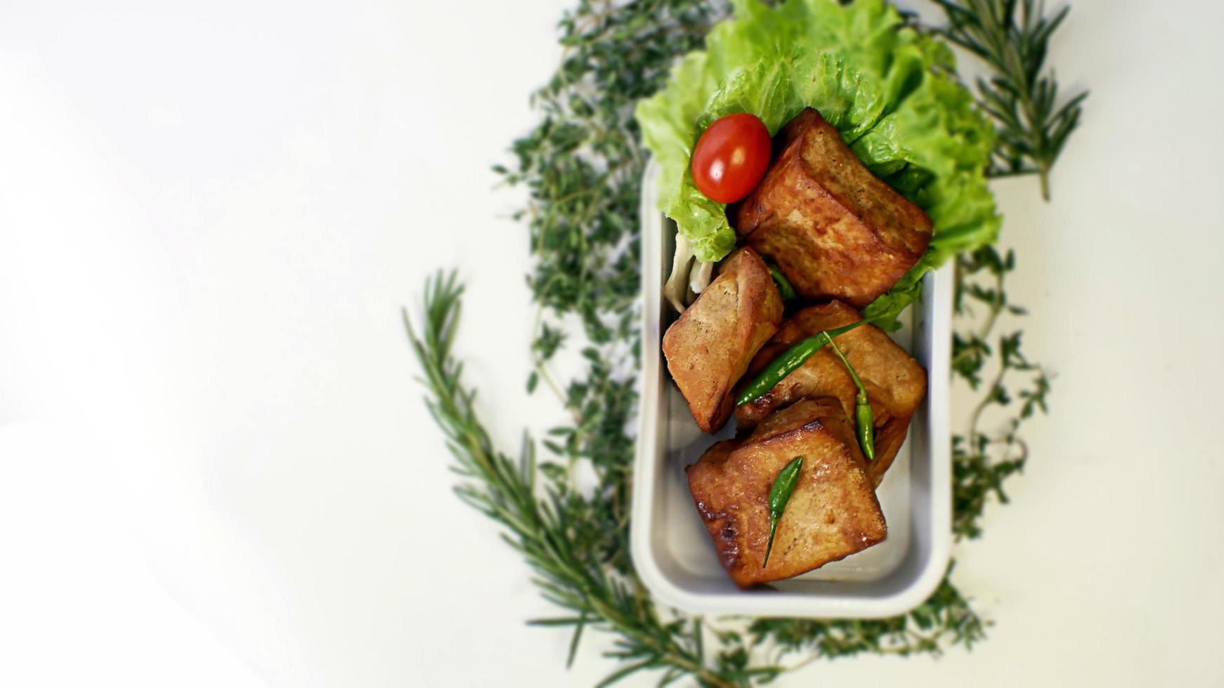 Fried tofu, small tomatoes and green chilies along with lettuce in one aluminum container, Indonesian street food on a white background photo