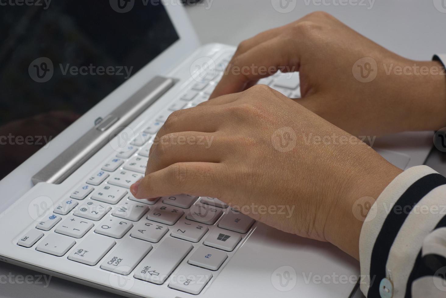 woman sitting at desk typing on the keyboard of a white laptop photo