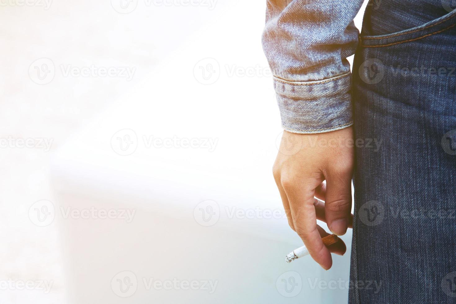 man holding smoking a cigarette in hand. Cigarette smoke spread. dark background photo