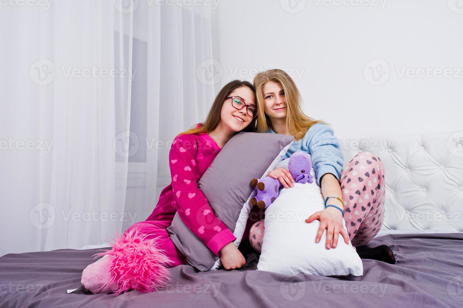Two friends girls in pajamas having fun on bed at room. photo