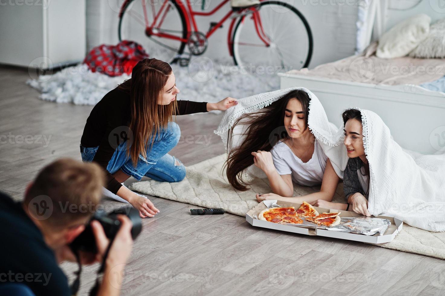 Man photographer shoot on studio twins girls who are eating pizza. Assistant helps in shooting. Professional photographer on work. photo