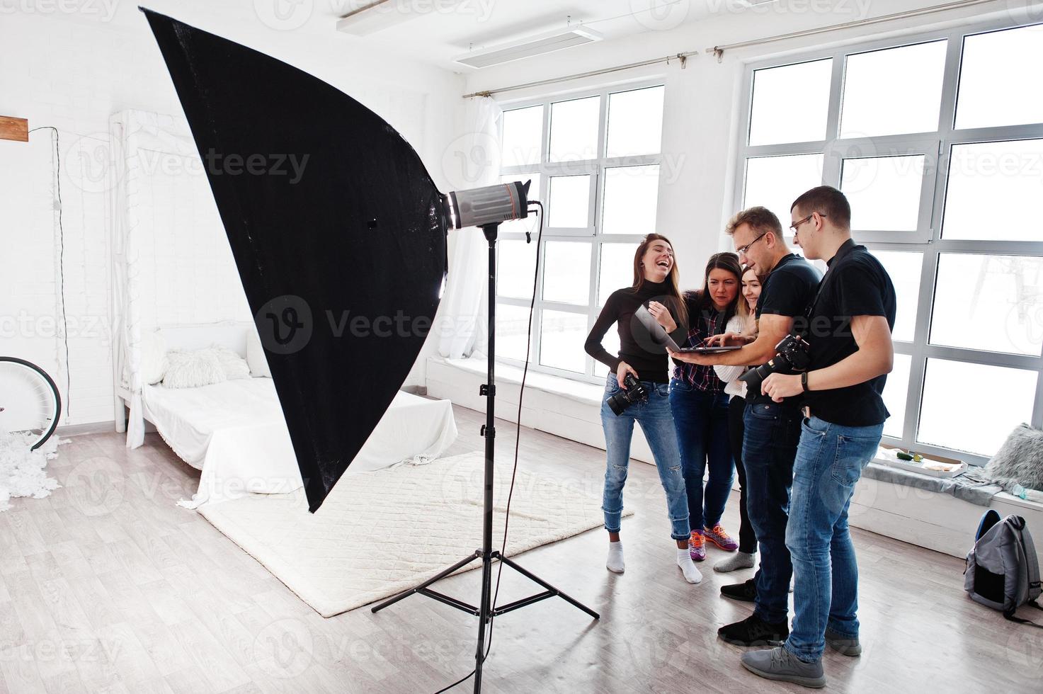 Photographer explaining about the shot to his team in the studio and looking on laptop. Talking to his assistants holding a camera during a photo shoot. Teamwork and brainstorm.