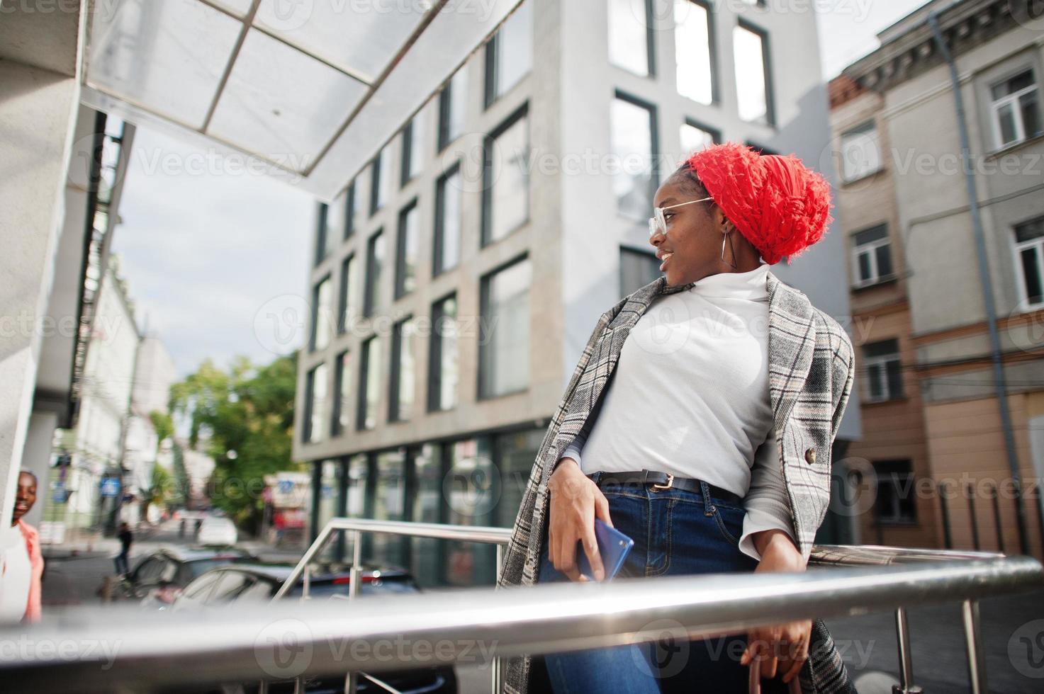 joven mujer musulmana africana moderna, atractiva, alta y delgada con hiyab o pañuelo en la cabeza con turbante habla por teléfono móvil contra la ciudad. foto