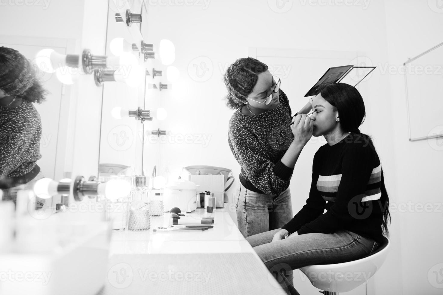 African American woman applying make-up by make-up artist at beauty saloon. photo