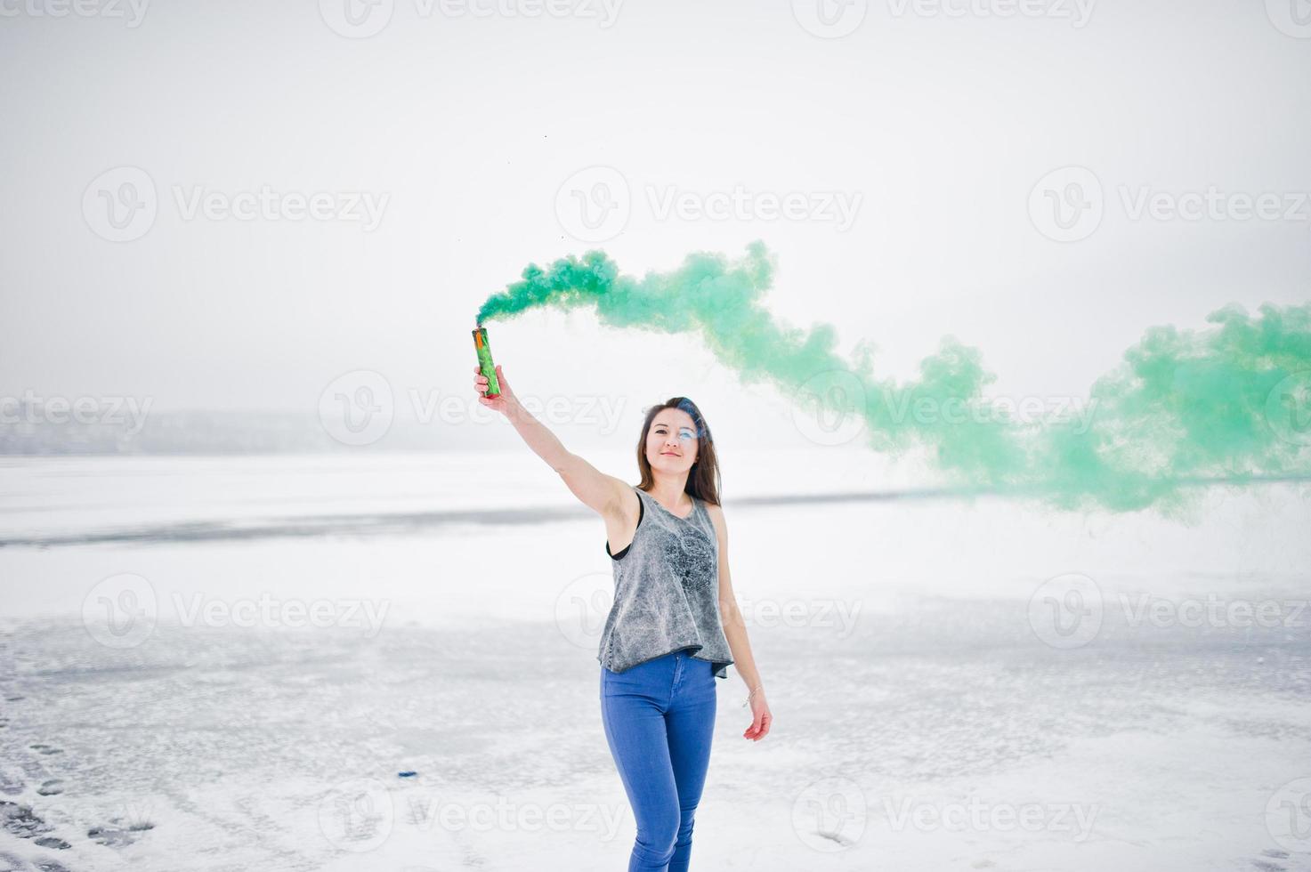 Young girl with green colored smoke bomb in hand in winter day. photo